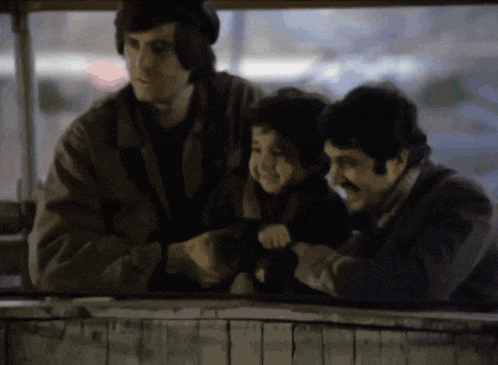 a man holds a small child while another man looks on