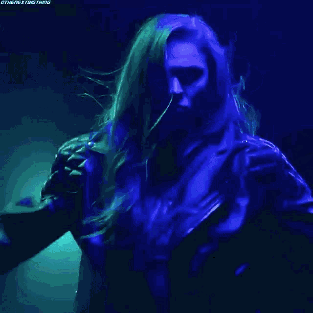 a woman is singing into a microphone in a dark room with blue lights behind her .