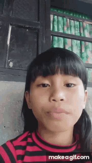 a girl in a red and black striped shirt is making a face