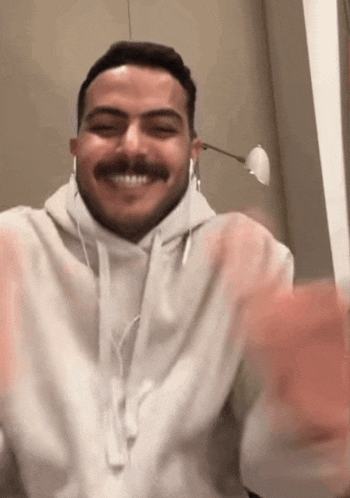 a man with a mustache wearing headphones and a white hoodie is smiling