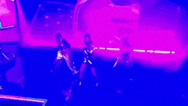 a group of women are dancing on a stage with purple lights