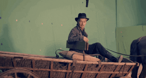 a man in a hat sits in a wagon with a green background