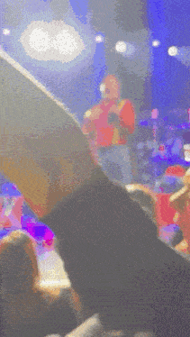 a man in a red shirt is singing into a microphone