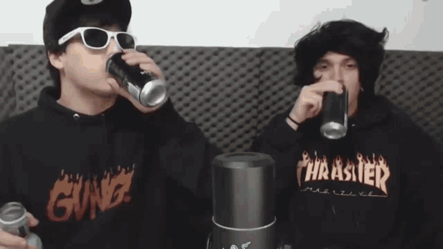 a man wearing a thrasher hoodie drinks from a can