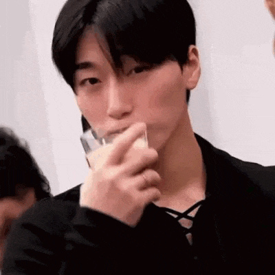 a young man is drinking from a glass while looking at the camera .