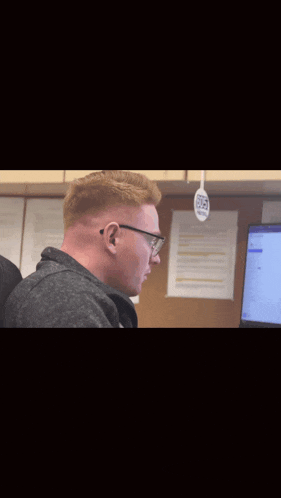 a bald man wearing glasses looks surprised in front of a computer monitor