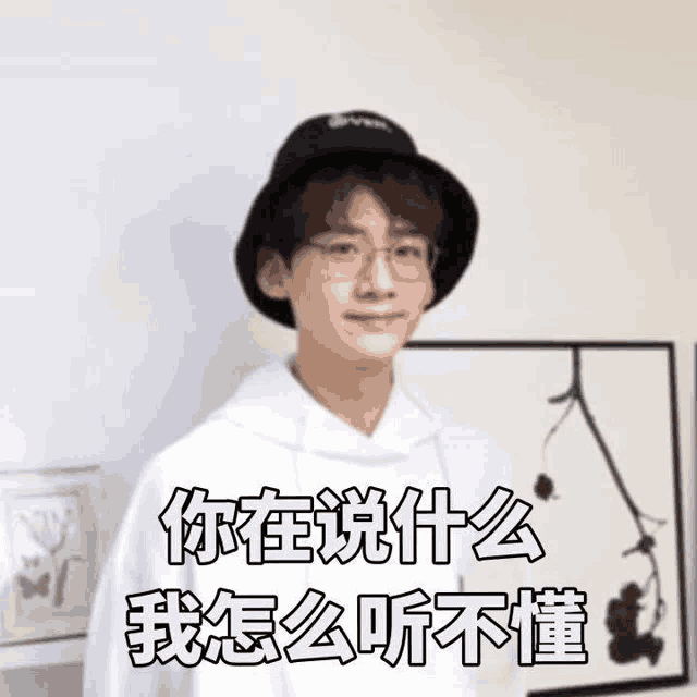 a young man wearing a hat and glasses is standing in front of a wall with chinese characters on it .