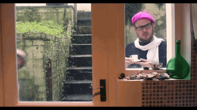 a man wearing a pink hat and glasses looks out a window