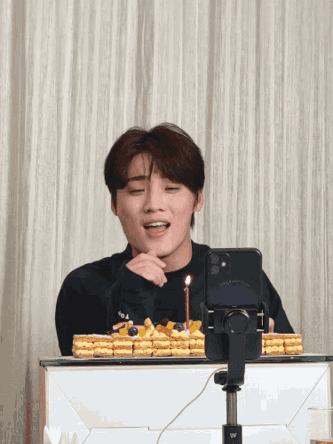 a young man sitting in front of a cake with a candle and a phone that says live and love