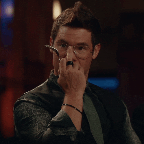 a man with glasses and a ring on his finger holds a fork in his mouth