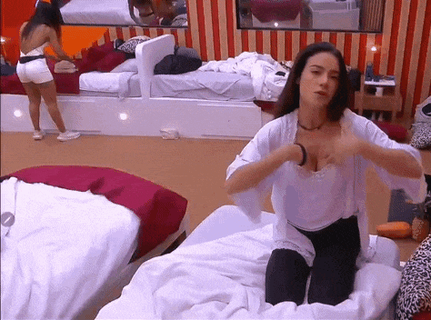 a woman is sitting on a bed and adjusting her breasts