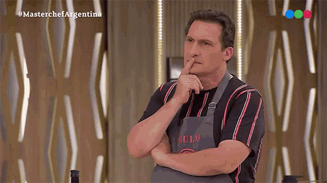 a man wearing an apron that says aulo holds his finger to his nose