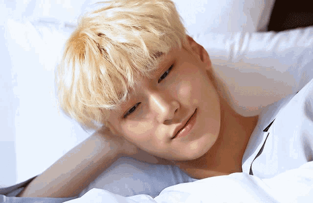 a young man with blonde hair is laying on a bed and smiling