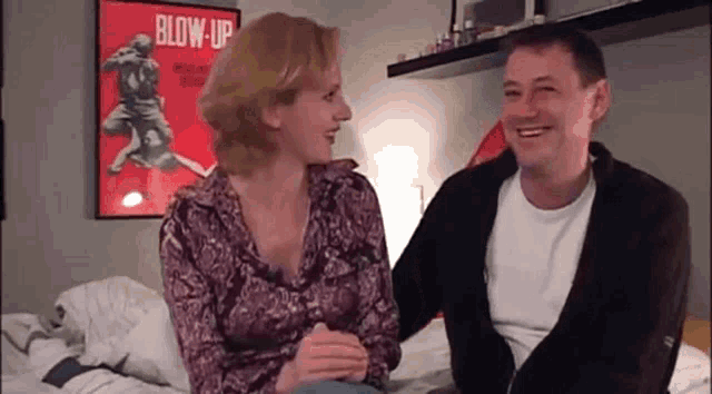 a man and woman are sitting on a bed in front of a blow up poster