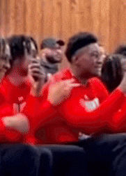 a group of people wearing red sweatshirts are sitting in a row and applauding .