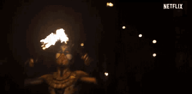 a man with a mask is holding a fire torch in front of a crowd .