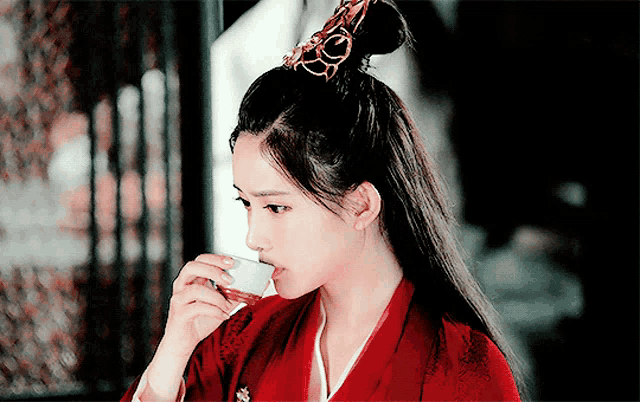a woman in a red kimono drinking from a small cup