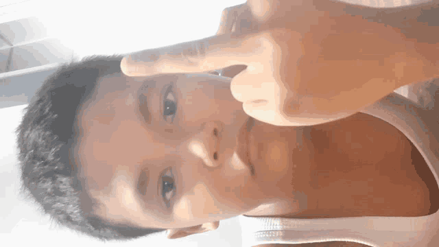 a young boy wearing a white tank top is making a funny face