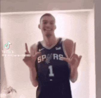 a man in a spurs jersey is making a funny face and giving the middle finger .