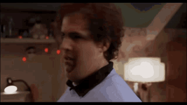 a man with curly hair is standing in a room with a lamp and making a funny face .