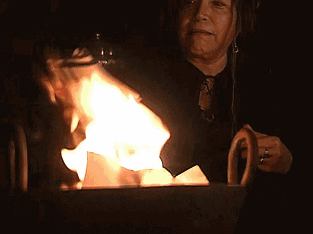 a woman stands in front of a large fire