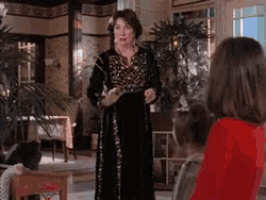 a woman in a black dress is standing in a living room with two girls