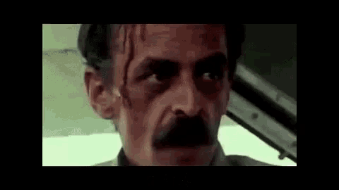 a man with a mustache is sitting in a car looking at the camera .