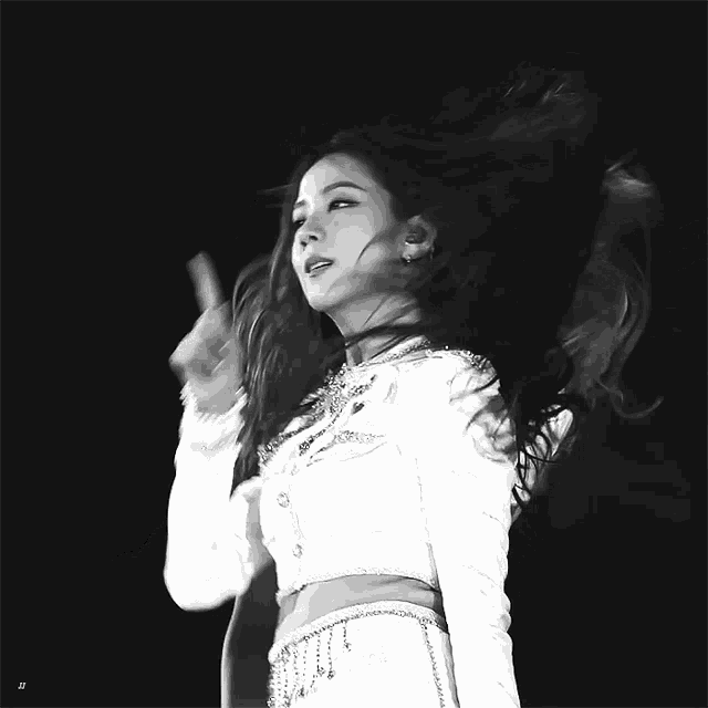 a black and white photo of a woman in a white dress with her hair blowing in the wind .