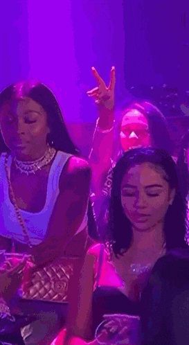 a group of women are sitting at a table in a club . one of the women is giving a peace sign .