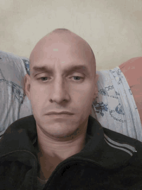 a man with a shaved head looks at the camera while laying on a bed