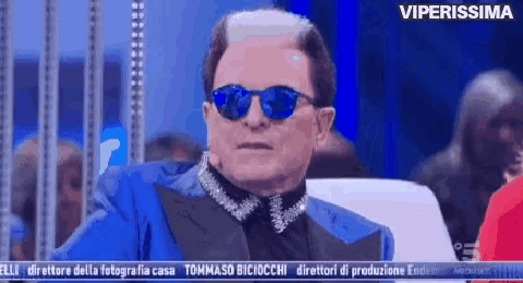 a man wearing sunglasses and a blue suit is sitting in front of a screen that says viperissima on it