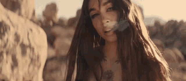 a woman with long hair is standing in the desert with rocks in the background