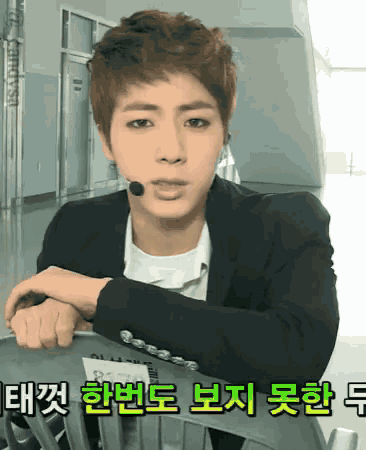 a man in a suit is leaning on a chair with korean writing on the bottom right