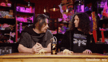two men are sitting at a table and one of them is wearing a shirt that says ground kontrol