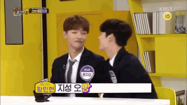 two men are sitting at a table and one of them is wearing a name tag that says kbs2