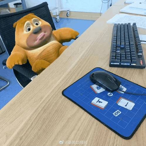 a teddy bear laying on a desk next to a keyboard and mouse