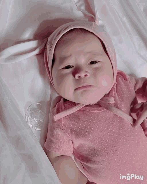 a baby wearing a pink hat is laying on a bed with a pacifier