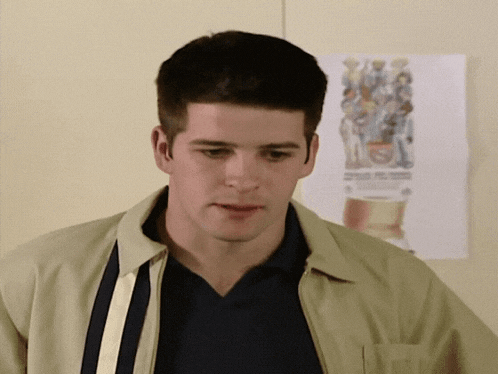 a man in a tan jacket stands in front of a poster on the wall