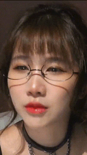 a girl wearing glasses and a choker is looking at the camera