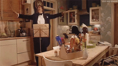 a man in a tuxedo is standing in a kitchen with his arms outstretched .
