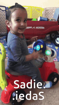 a little boy is riding a red toy car with the words sadie iedas written on the bottom