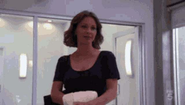 a woman in a blue shirt is standing in a room with the number 5 on the wall behind her