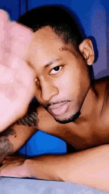 a shirtless man with a tattoo on his forehead is laying on a bed and looking at the camera .