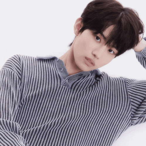 a young man wearing a striped shirt is laying down with his hand in his hair