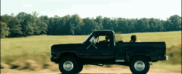 a black truck is driving down a dirt road with trees in the background