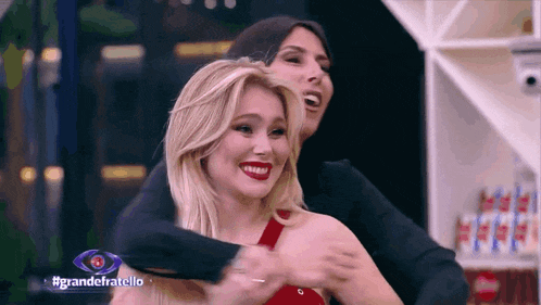 two women are hugging each other in front of a sign that says grande fratello