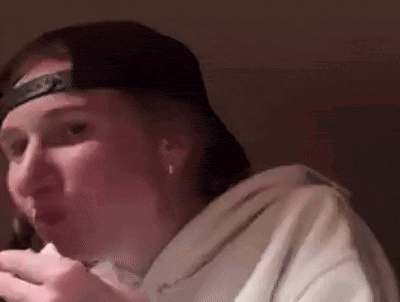 a woman wearing a baseball cap and a white hoodie is eating a piece of food .