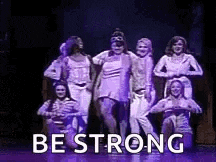 a group of women are dancing on a stage with the words `` be strong '' written on it .