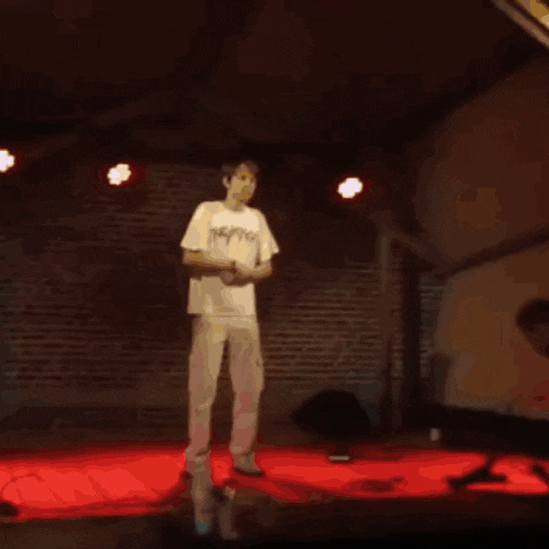 a man in a white shirt stands on a stage with his arms in the air