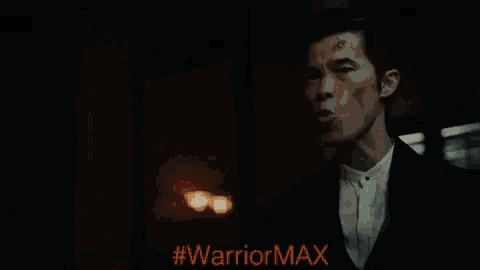 a man in a suit and hat stands in a dark room with #warriormax written on the bottom